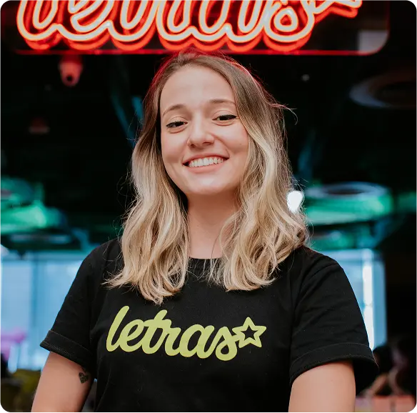 Foto da autora Laryssa Magalhães, com cabelos loiros e blusa preta estampada com o logo do Letras.